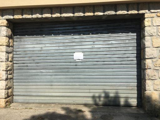 Porte de garage en acier Porte de garage grise en métal, avec une affiche blanche collée au centre.