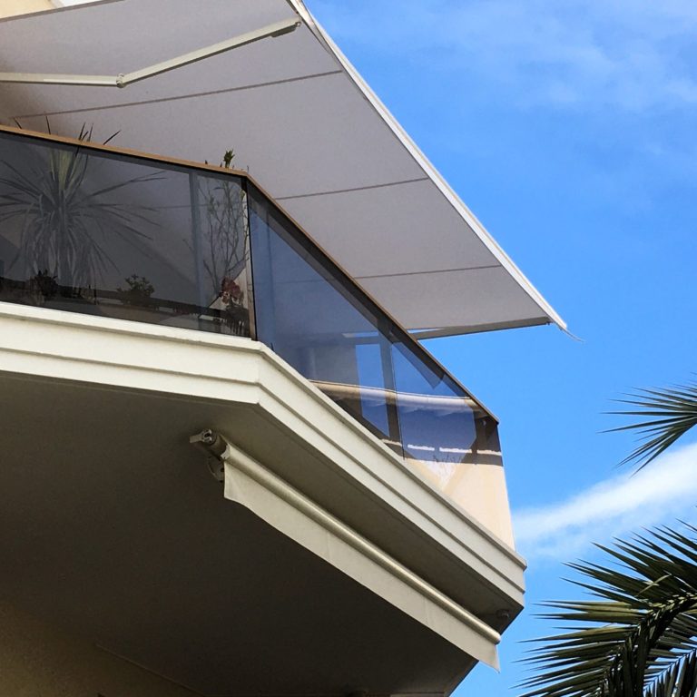 Store de balcon Somfy Balcon avec auvent, vue sur le ciel bleu et des palmiers à proximité.