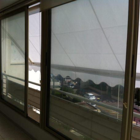 Baie coulissante avec store extérieur Vue sur un balcon avec des rideaux et une toile tendue, près d'une route.